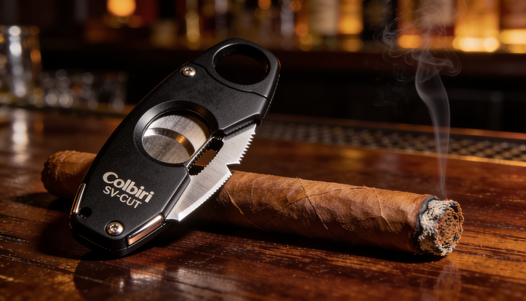 Colibri SV-Cut two-in-one cigar cutter in black finish resting on a dark bar next to a premium cigar