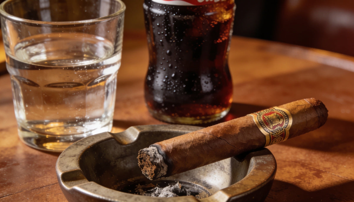 A premium cigar in an ashtray beside a glass of water and a soda, illustrating how to handle a cigar buzz